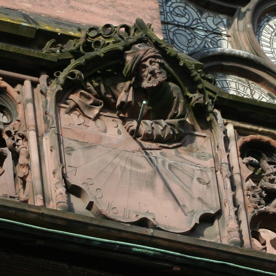 Relógio de sol de estilo polar da catedral de Estrasburgo. O antebraço esquerdo da personagem, pousado sobre a parte superior da mesa do relógio de sol, segura (ou segurava) o estilo na mão.